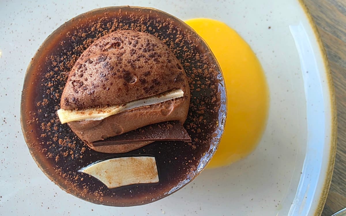 Chocolate mousse dusted with cocoa, with a pool of bright orange confit alongside, in the Spatisserie at Gaia Spa