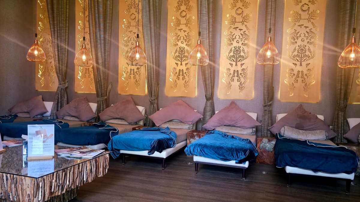 The post-treatment relaxation room at Gaia Spa: a row of beds with blue throws and blush cushions beneath gold panels and hanging lanterns